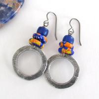 These handcrafted earrings feature silver pewter circle hoops with a hand stamped texture accented with colorful African glass beads and navy blue glass beads. They have an earthy, boho style and are lightweight and comfortable to wear.  MEASUREMENTS: Total length 2" from top of gray silver niobium (hypoallergenic) ear wires and 1” at widest point. The circles were created out of solid lead-free pewter; hand stamped and oxidized; and signed on the back with my initials.