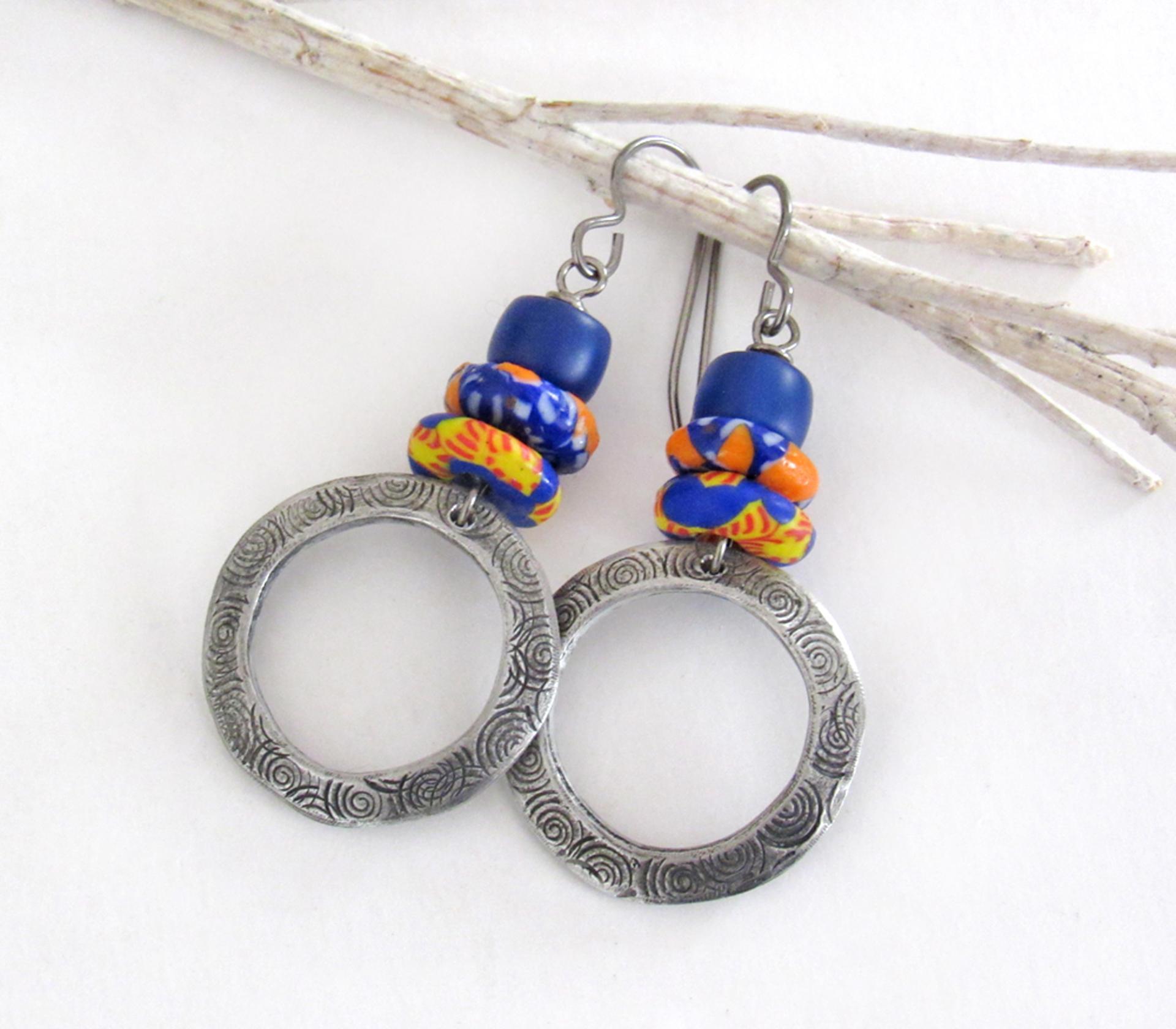These handcrafted earrings feature silver pewter circle hoops with a hand stamped texture accented with colorful African glass beads and navy blue glass beads. They have an earthy, boho style and are lightweight and comfortable to wear.  MEASUREMENTS: Total length 2" from top of gray silver niobium (hypoallergenic) ear wires and 1” at widest point. The circles were created out of solid lead-free pewter; hand stamped and oxidized; and signed on the back with my initials