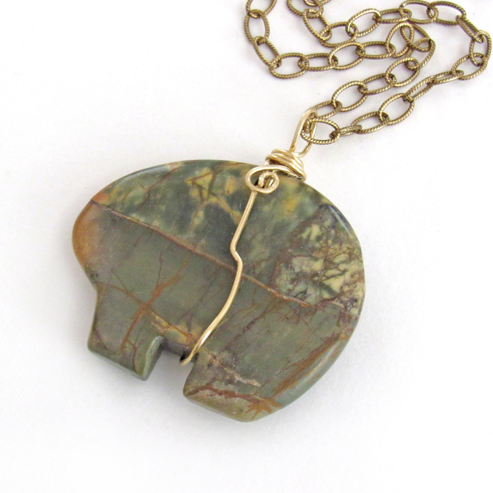 This pendant necklace features a large natural Red Creek jasper stone carved into a southwestern zuni bear shape. It's wrapped in gold brass wire and hangs from a textured brass chain. The stone has an earthy mossy green hue with subtle accents of yellow and streaks of brown. The style is unisex - perfect for a man or woman. One of a kind - it makes a great gift for a rock hound - or zuni bear lover.